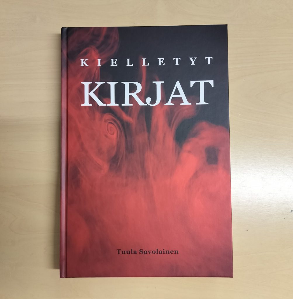 Vaalealla pöydällä Kielletyt kirjat -teos, jonka kannessa tulen punaisia loimuja.